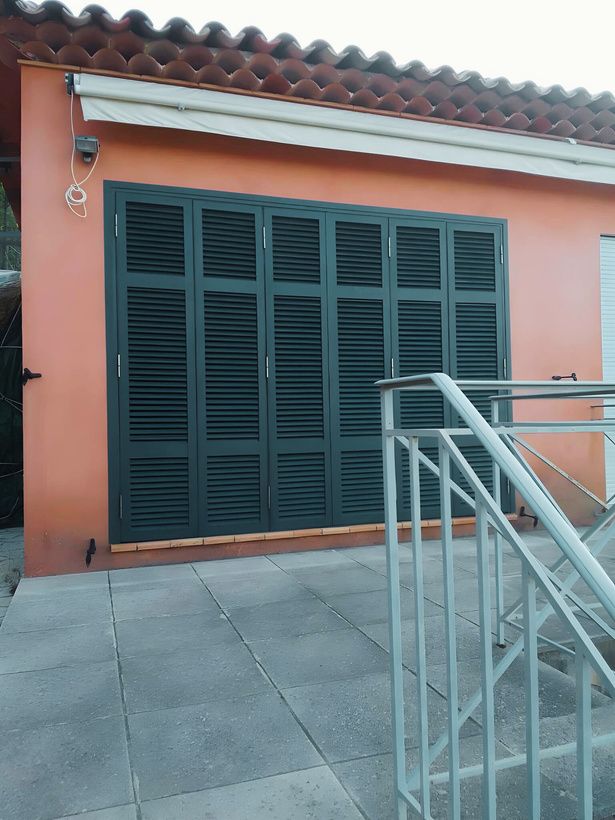 Persiennes aluminium vertes sur une façade rosée